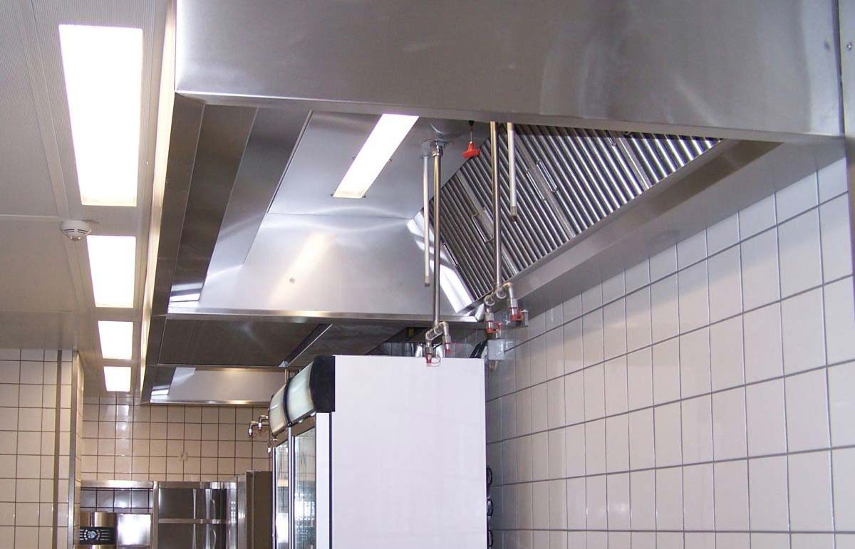 Eine große Edelstahl-Abzugshaube mit integrierter Beleuchtung und Brandschutzsystem in einer Gastronomieküche.