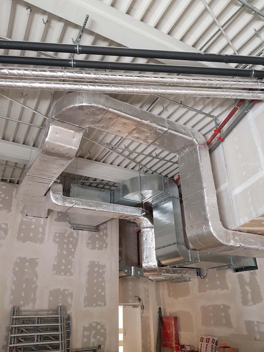 Installation von isolierten und unisolierten rechteckigen Lüftungskanälen in einem Rohbau für eine Luftanlage.