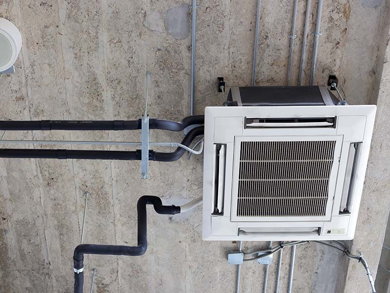Deckenkassetten-Klimaanlage mit isolierten Rohrleitungen und Elektroverkabelung in einem Büro installiert.